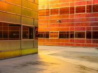 an industrial building with orange colored windows, with rain falling on the floor, along with a bench to sit out front