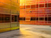 an industrial building with orange colored windows, with rain falling on the floor, along with a bench to sit out front