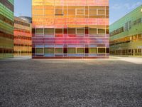 an orange and blue building with windows that have a rainbow pattern on the outside and two green buildings on the inside