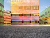 an orange and blue building with windows that have a rainbow pattern on the outside and two green buildings on the inside