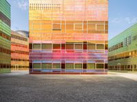 an orange and blue building with windows that have a rainbow pattern on the outside and two green buildings on the inside