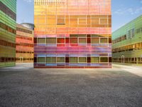 an orange and blue building with windows that have a rainbow pattern on the outside and two green buildings on the inside