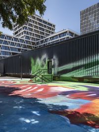 an outside mural with bright colours is painted on a park bench in front of large building