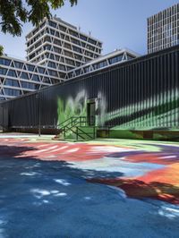 an outside mural with bright colours is painted on a park bench in front of large building