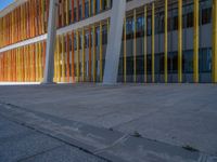 a concrete structure made into rows of orange and yellow poles are on a cement sidewalk
