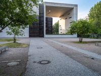 a building sits next to green trees and some gray bricks in the ground on which is a small cobble stone area