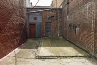 a narrow alley with brick buildings and door on one side of the road and brick wall on other side