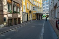 a very narrow alley with some buildings and one man on the sidewalk using a phone