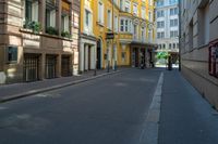 a very narrow alley with some buildings and one man on the sidewalk using a phone