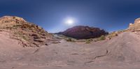 a panoramic view of a narrow river in the desert with red rocks, shrubs and a blue sky