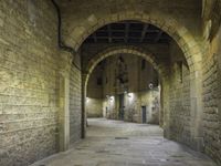 an arched hallway leading to three buildings in a stone area with brick walls and ceilinging