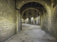 an arched hallway leading to three buildings in a stone area with brick walls and ceilinging