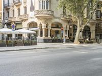 a narrow city street lined with tall trees and restaurants in an upscale area in the background