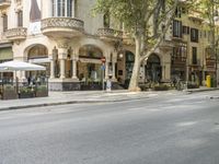 a narrow city street lined with tall trees and restaurants in an upscale area in the background