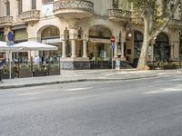 a narrow city street lined with tall trees and restaurants in an upscale area in the background