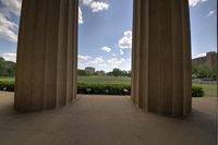 looking through the pillars to the field of green trees and flowers, with a building in the back ground