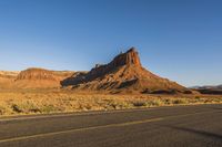 a desert landscape with red rocks and white lines along a long road leading to a mountain