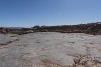 an arid area with some rocks and mountains in the background a bright blue sky is visible