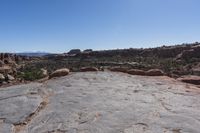 an arid area with some rocks and mountains in the background a bright blue sky is visible