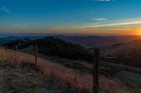 there is a sunset in the horizon on a field with grassy land below the mountains