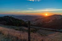 there is a sunset in the horizon on a field with grassy land below the mountains