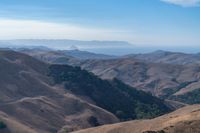 a person on a mountain top looks at a distant valley below mountains, beneath a blue sky