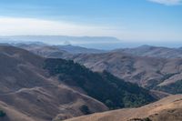 a person on a mountain top looks at a distant valley below mountains, beneath a blue sky