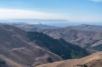 a person on a mountain top looks at a distant valley below mountains, beneath a blue sky