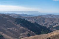 a person on a mountain top looks at a distant valley below mountains, beneath a blue sky