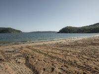 an empty beach near a wooded shore line with footprints in the sand and the water in the background