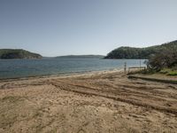 an empty beach near a wooded shore line with footprints in the sand and the water in the background