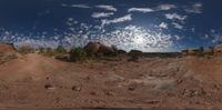 a 360 - view of a dirt road surrounded by mountains with sun shining in the distance