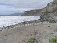 a man stands on the shore and looks out to sea with a small purple umbrella