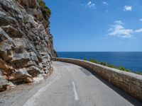 a curved mountain road that curves away from the ocean and next to the wall is a rock cliff