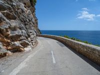 a curved mountain road that curves away from the ocean and next to the wall is a rock cliff