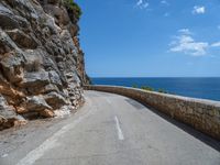 a curved mountain road that curves away from the ocean and next to the wall is a rock cliff