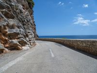 a curved mountain road that curves away from the ocean and next to the wall is a rock cliff