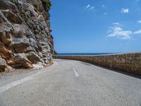 a curved mountain road that curves away from the ocean and next to the wall is a rock cliff