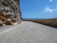 a curved mountain road that curves away from the ocean and next to the wall is a rock cliff