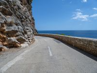 a curved mountain road that curves away from the ocean and next to the wall is a rock cliff