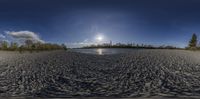 a beach with water near some trees and a sun light over it is shown in a fish - eye picture