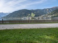 a man with a hat walks in the grass near some water and a lake with mountains in the background