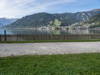 a man with a hat walks in the grass near some water and a lake with mountains in the background