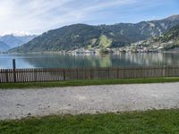 a man with a hat walks in the grass near some water and a lake with mountains in the background