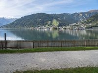 a man with a hat walks in the grass near some water and a lake with mountains in the background