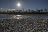 the sun is shining over rocks in the middle of a river, as water and trees line the bank