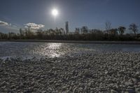 the sun is shining over rocks in the middle of a river, as water and trees line the bank