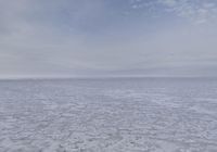 a lone snow covered ocean surrounded by snow and cloudy skies with blue sky in the background