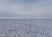 a lone snow covered ocean surrounded by snow and cloudy skies with blue sky in the background