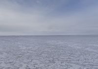 a lone snow covered ocean surrounded by snow and cloudy skies with blue sky in the background